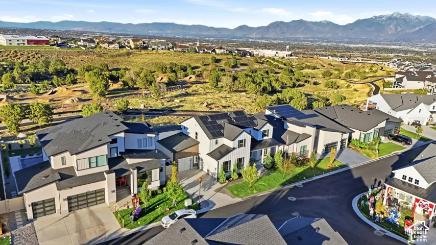 Aerial perspective of modern multi-story residential structures featuring integrated solar panel arrays, multi-car garages, composite roofing, and mountain backdrops