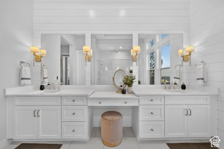 Double vanity featuring white cabinetry, quartz countertops, undermount sinks, shiplap wall detailing, and gold-finish wall sconces