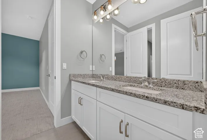 Double vanity with stone-surface countertop, dual integrated rectangular sinks, white shaker-style cabinetry, and multi-bulb linear vanity lighting