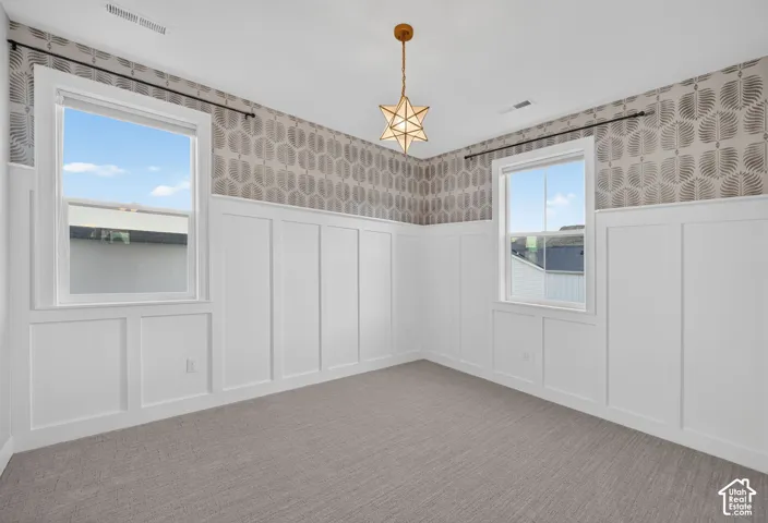 Room featuring floor-to-ceiling wainscoting, geometric patterned wallcovering, neutral carpeting, and a multi-point star pendant light fixture