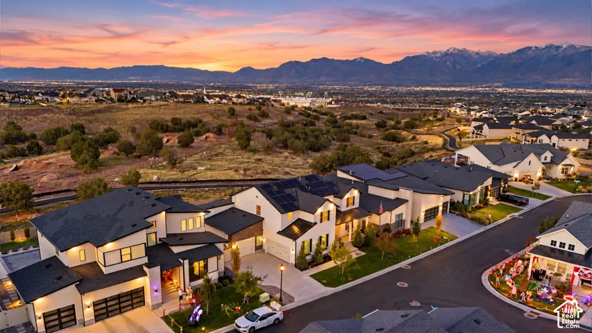 Multi-level residential architecture featuring light-toned exterior siding, dark-toned shingle roofing, integrated solar panels, and multi-car garages, set against a mountainous backdrop