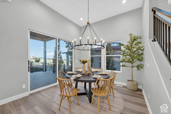 Dining area featuring vaulted ceilings, wide-plank wood-finish flooring, a contemporary iron-frame chandelier, and a sliding glass door providing external deck access