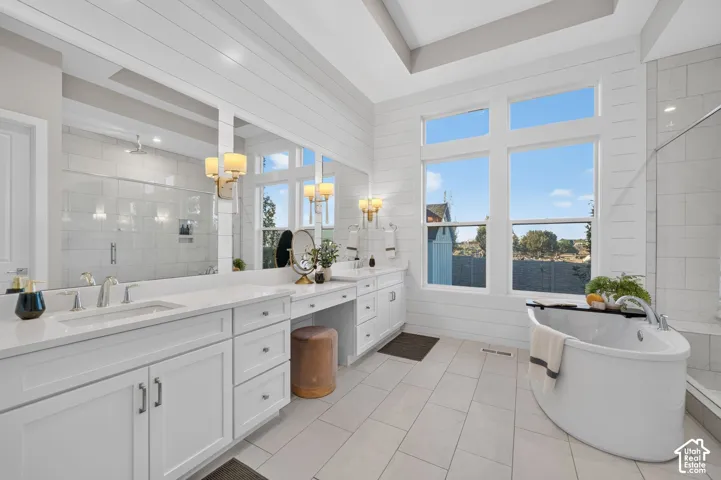 Bathroom featuring shiplap walls, a dual-sink vanity with stone-surfaced countertops, a freestanding soaking tub, and large-format tile flooring