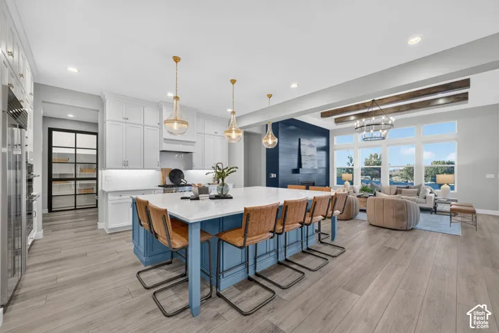 Kitchen featuring a center island with a stone countertop, white cabinetry, wood-finish flooring, exposed ceiling beams, and a walk-in pantry with a black-frame glass door