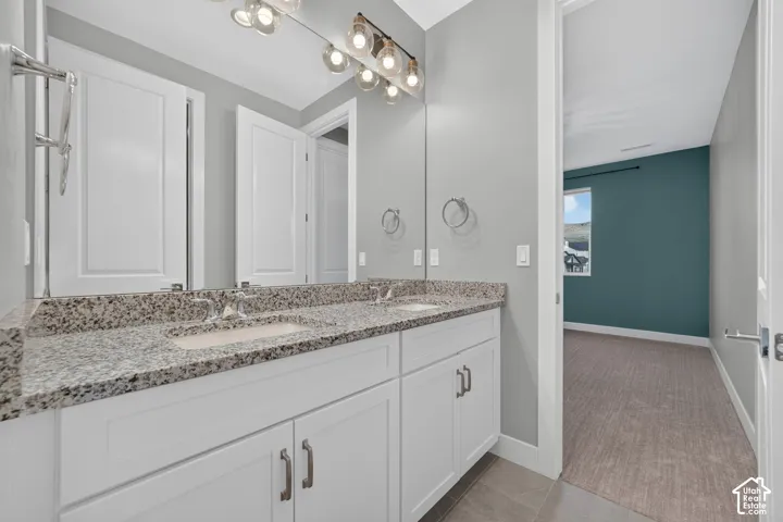 Double vanity featuring white cabinetry, stone-finish countertops, undermount sinks, and a full-width mirror with a multi-bulb light fixture