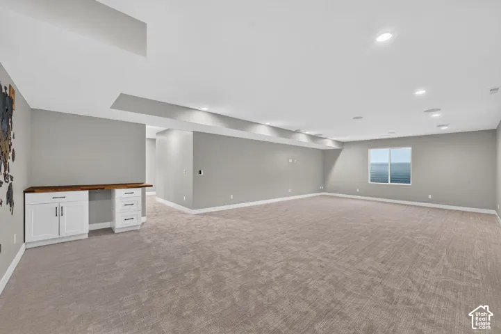 Spacious open-concept interior featuring recessed lighting, wall-to-wall carpeting, and a built-in workstation with shaker-style cabinetry and a wood-finish countertop