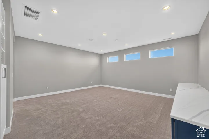 Room featuring recessed lighting, carpeted flooring, three high-set rectangular windows, and a built-in cabinet with a stone-finish countertop