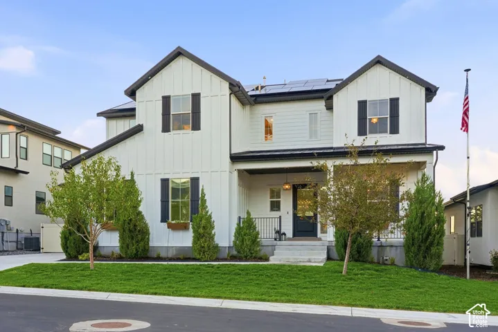 Two-story farmhouse-style exterior featuring vertical board-and-batten siding, dark shutters, a covered front porch with metal roofing, and roof-mounted solar panels