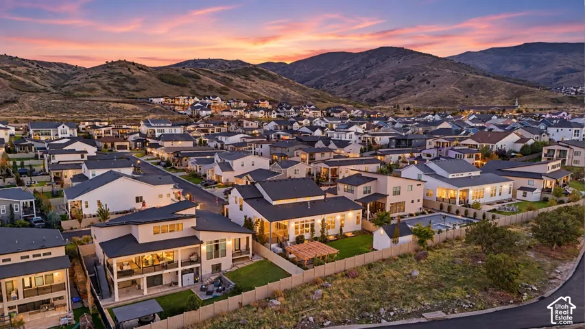 Aerial perspective featuring residential lots with manicured lawns, fenced perimeters, covered patios, and pergola structures set against a prominent mountain backdrop