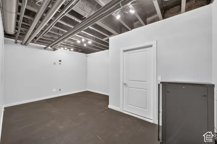 Finished interior space featuring exposed ceiling joists, industrial-style exposed mechanical ductwork, track lighting, dark matte flooring, and a solid-core interior door