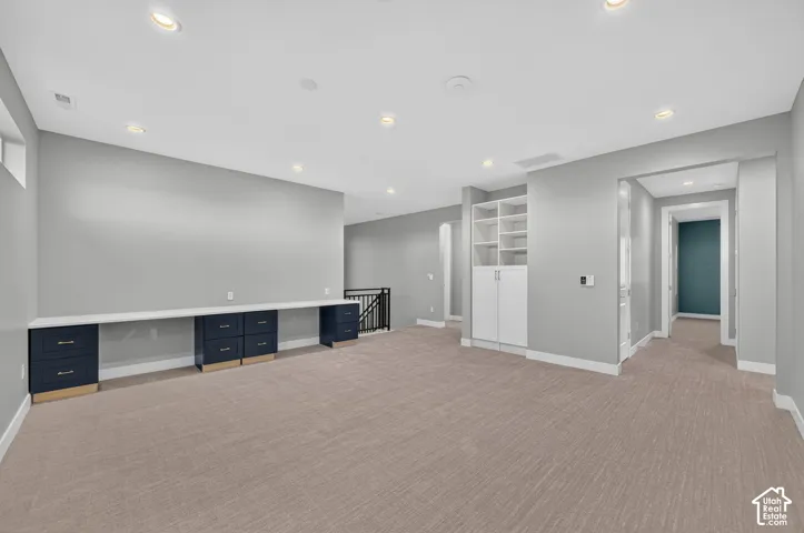 Open-concept area featuring neutral carpeting, recessed lighting, built-in desk cabinetry with a solid surface countertop, and floor-to-ceiling shelving