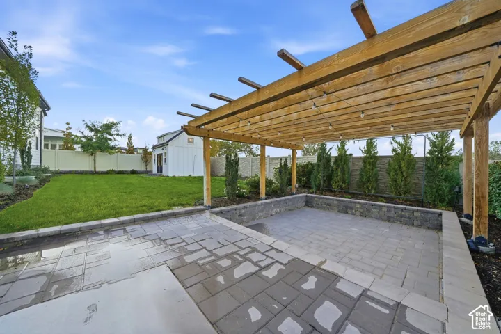 Outdoor space featuring a custom wood pergola, paved stone patio, perimeter stone retaining wall, manicured lawn, and detached structure