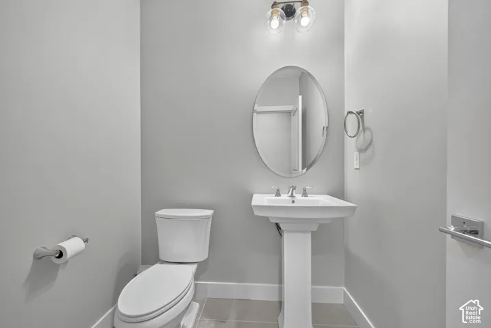 White pedestal sink with chrome faucet, oval wall-mounted mirror, two-light fixture with glass globes, and tile flooring