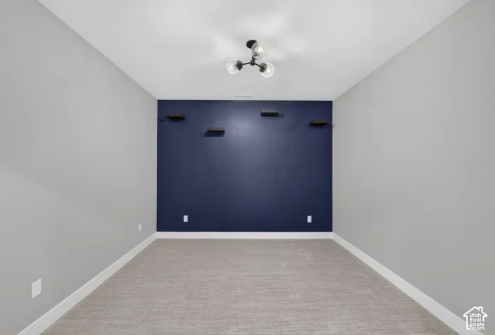 Room featuring an accent wall, four built-in floating shelves, neutral wall-to-wall carpeting, and a multi-bulb flush-mount light fixture