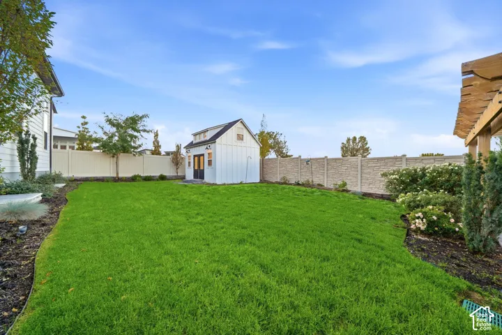 Backyard featuring a manicured lawn, detached board-and-batten storage structure, perimeter privacy fencing, and wood-beam pergola