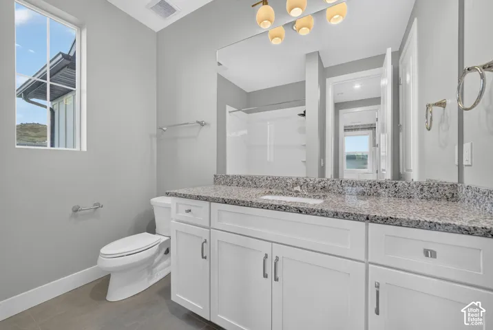Bathroom featuring white shaker-style cabinetry, stone-surface countertop with an integrated basin, large-format mirror, multi-light fixture, and ceramic tile flooring