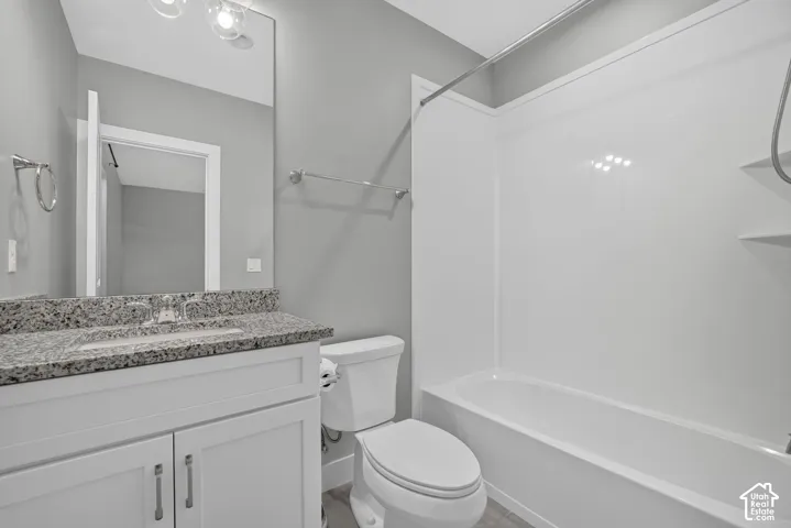 Bathroom featuring a vanity with stone-finish countertop, undermount sink, full-height wall mirror, and a tub-shower combination with integrated shelving