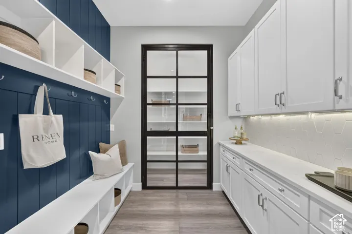 Custom built-in storage bench with vertical plank wall detailing, white cabinetry with countertop workspace, hexagonal tile backsplash, and a glass-paneled metal-frame door