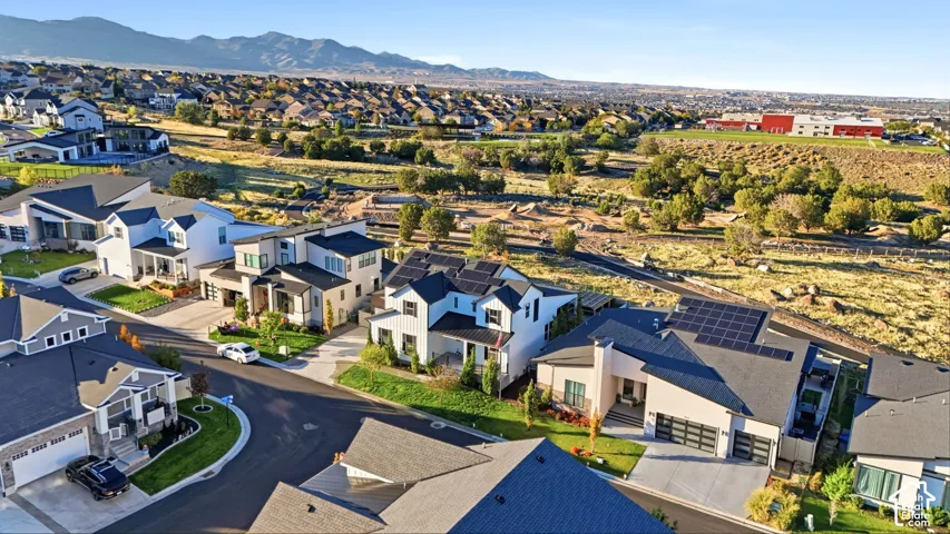 Aerial view of residential neighborhood featuring modern multi-level homes, solar panel arrays, attached multi-car garages, concrete driveways, and mountain backdrop