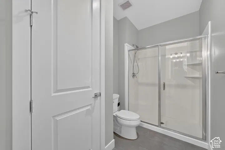 Bathroom featuring a glass-enclosed shower, integrated shelving, handheld shower fixture, and tiled flooring