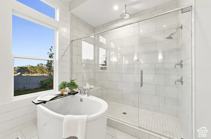 Freestanding oval soaking tub, glass-enclosed walk-in shower with floor-to-ceiling tile, dual shower heads including a ceiling-mounted rainfall fixture, and large transom window