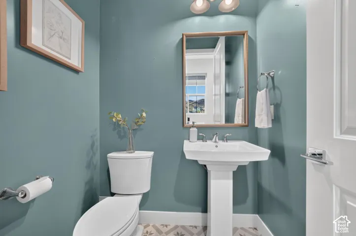 Powder room featuring a pedestal sink, metallic-finished faucet, framed wall mirror, patterned tile flooring, and polished chrome hardware