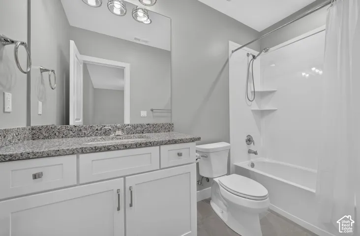 Bathroom featuring a white shaker-style vanity with stone-finish countertop, undermount sink, three-light fixture, and a tub-shower combination with built-in shelving