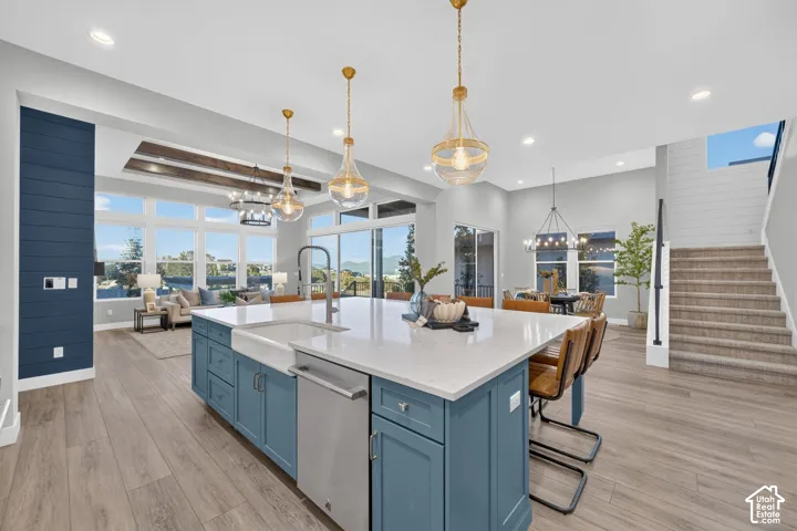 Kitchen featuring an oversized island with a farmhouse sink, quartz countertops, wood-finish flooring, decorative ceiling beams, and pendant lighting