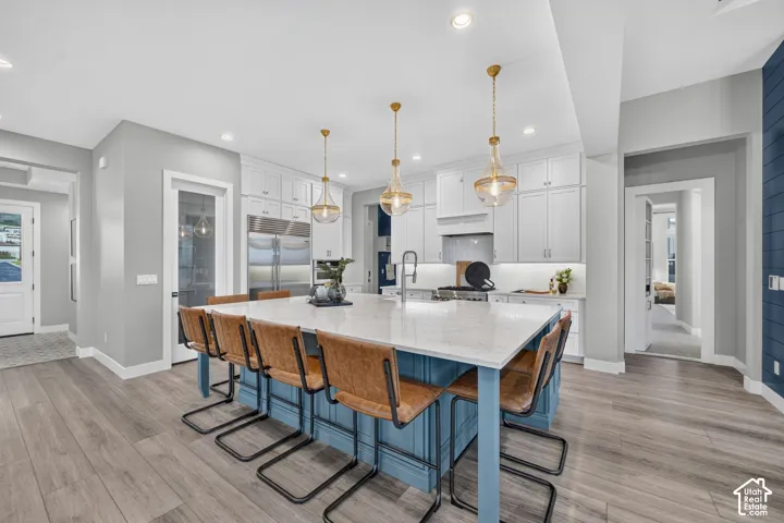 Kitchen featuring custom cabinetry, a large central island with a stone-finish countertop, stainless steel appliances, pendant lighting, and wood-finish flooring