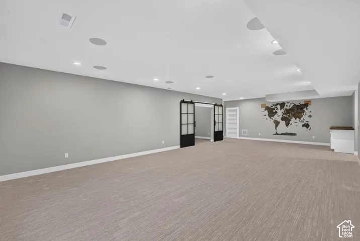 Open-concept space featuring recessed lighting, integrated ceiling speakers, carpeting, and black-framed sliding barn doors