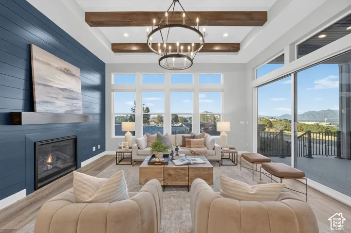 Living area featuring a tray ceiling with exposed wood beams, a fireplace with a horizontal shiplap surround, wood-finish flooring, and large windows with a mountain backdrop