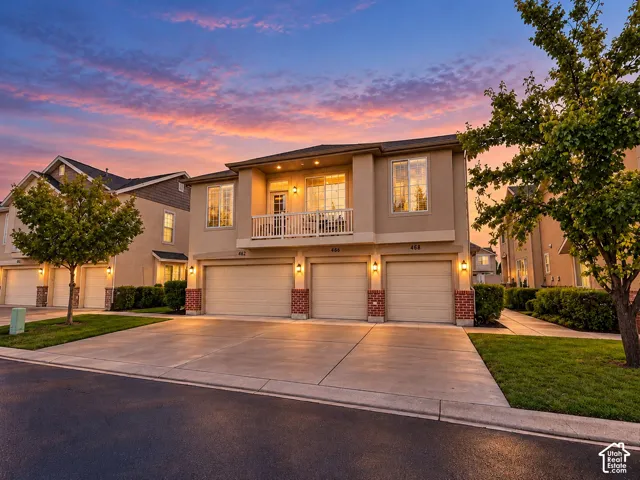 Multi-unit residence featuring a three-car garage, upper-level balcony with metal railing, stucco exterior with brick accents, and concrete driveway