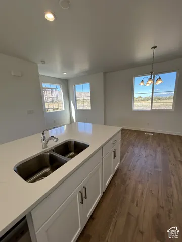 Kitchen island with stone-surface countertop, dual-basin stainless steel sink, white cabinetry, wood-finish flooring, and multi-light chandelier