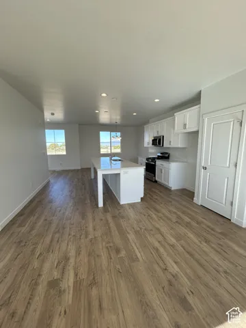 Kitchen featuring white cabinetry, quartz-surface center island, stainless steel appliances, recessed ceiling lighting, and wood-finish flooring