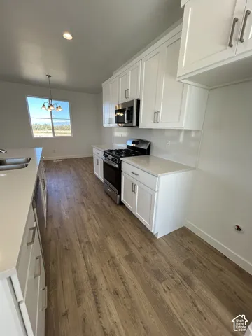Kitchen featuring white shaker cabinetry, light-toned composite countertops, stainless steel appliances, and wood-finish flooring