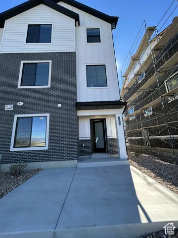 Three-story exterior featuring a mix of dark brick veneer and white vertical board-and-batten siding, a covered entryway, and a concrete driveway