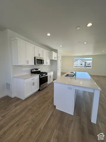 Kitchen featuring white shaker-style cabinetry, quartz countertops, a central island with a double-basin undermount sink, stainless steel appliances, and wood-finish flooring