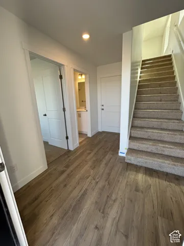 Interior entry featuring wood-finish flooring, recessed lighting, carpeted staircase with a white handrail, and shaker-style interior doors