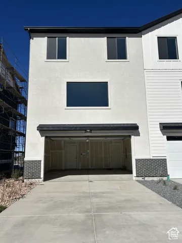 Three-story exterior featuring a smooth-stucco finish, brick veneer detailing, a concrete driveway, and an open-bay garage