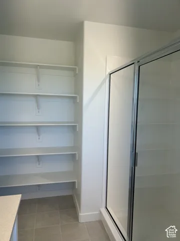 Shower enclosure with a chrome frame, multi-tier white wall-mounted shelving, and neutral tile flooring