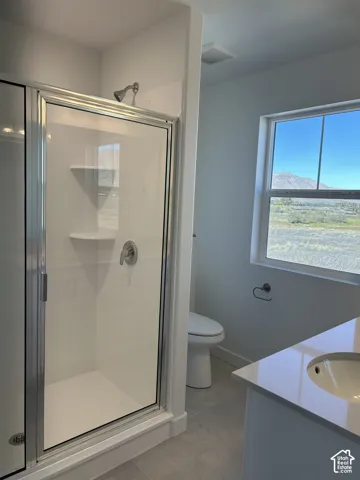 Bathroom featuring a shower stall with a glass door and built-in shelving, quartz-topped vanity, dual-flush toilet, and a window with mountain scenery