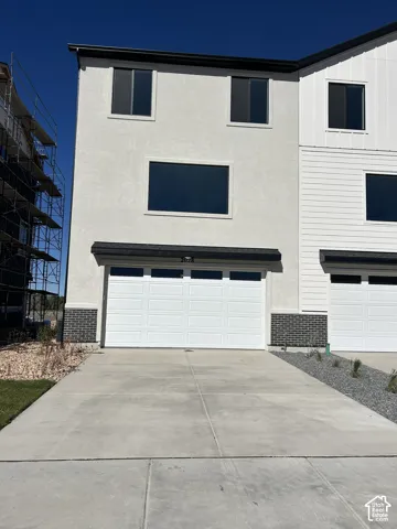 Multi-story exterior featuring a light-toned stucco facade, dark brick base detailing, and a multi-panel garage door