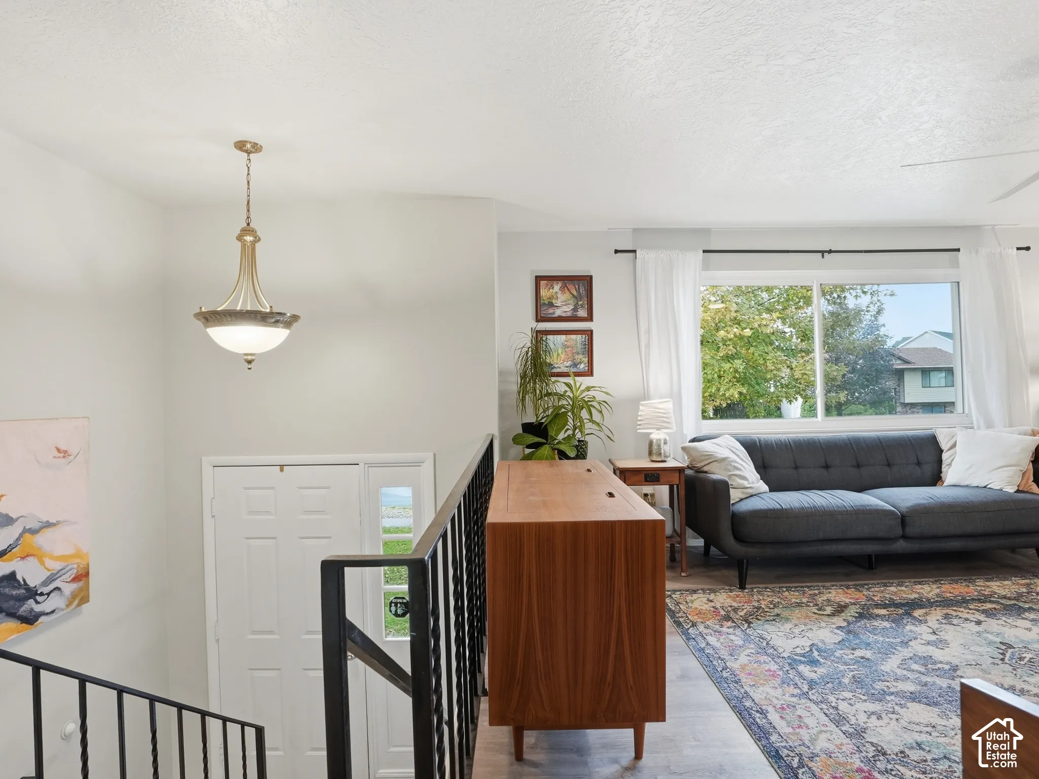 Open-concept interior featuring light-toned flooring, metal staircase railing, neutral wall color, and a decorative pendant light fixture