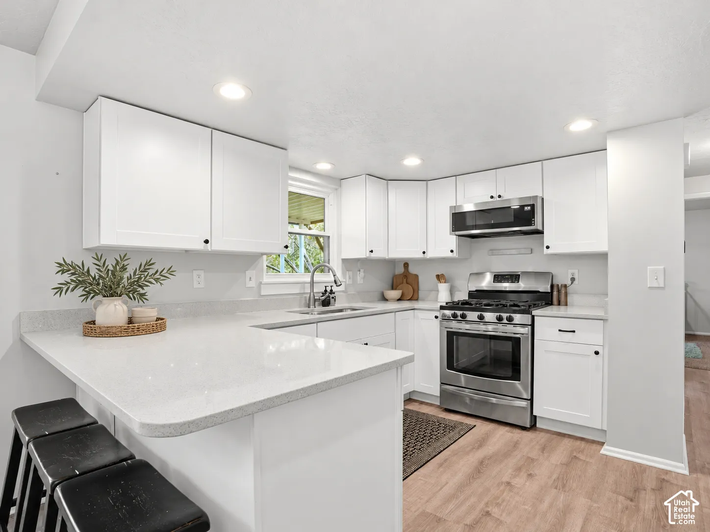 Kitchen featuring white shaker-style cabinetry, solid-surface countertops, stainless steel appliances, recessed ceiling lighting, and wood-finish flooring