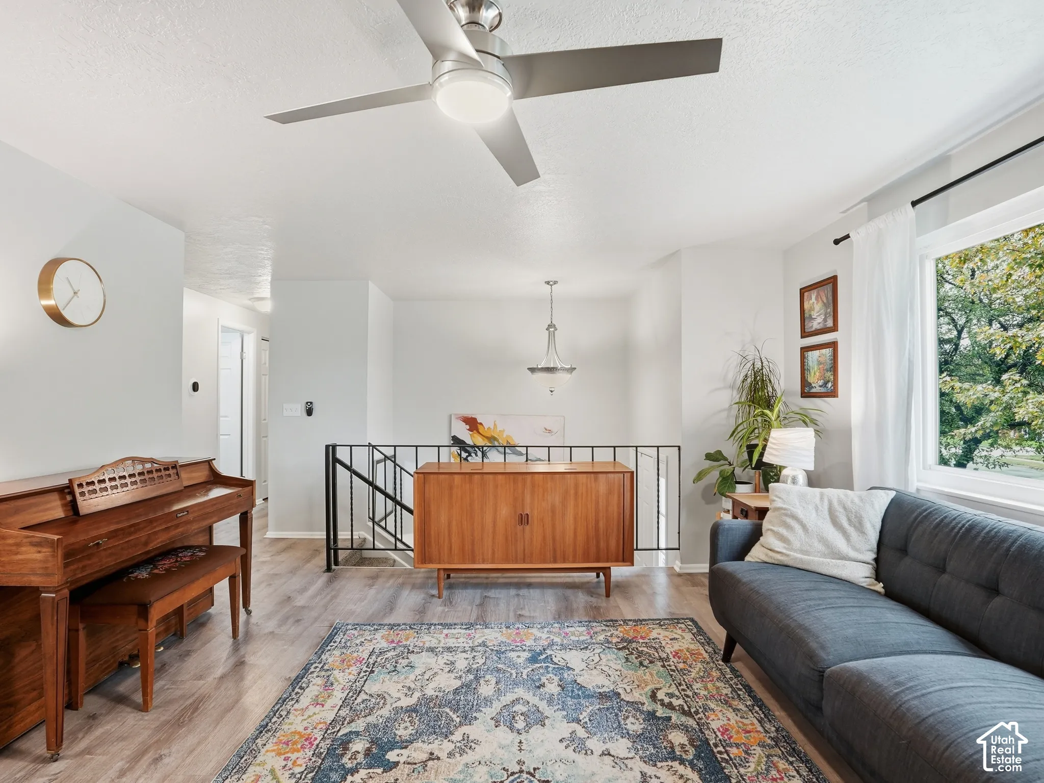 Wood-finish flooring, brushed metal ceiling fan with integrated lighting, and minimalist metal stair railing