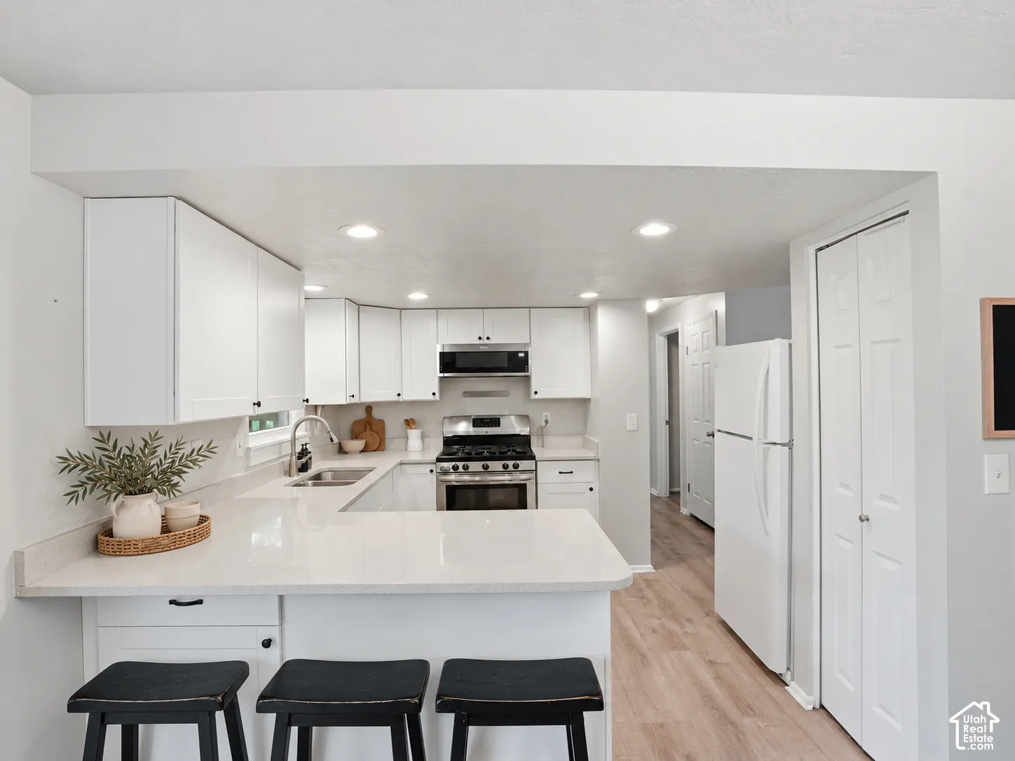 Kitchen featuring white shaker-style cabinetry, solid-surface countertops, a stainless steel gas range with overhead microwave, and wood-finish flooring