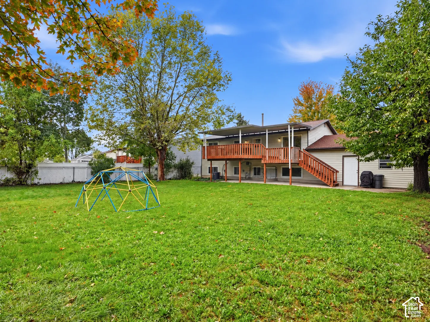 Backyard featuring a grass lawn, mature trees, wood deck with stairs, and white privacy fencing
