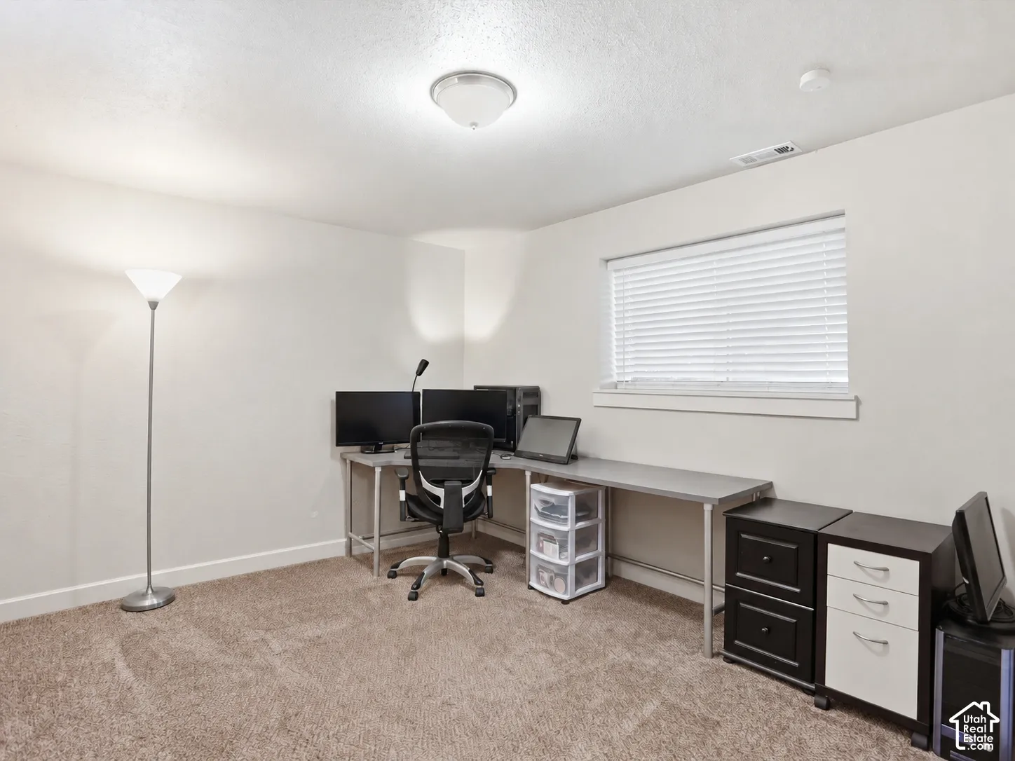 Neutral-toned interior space featuring wall-to-wall carpeting, a flush-mount ceiling light fixture, and a window with horizontal blinds