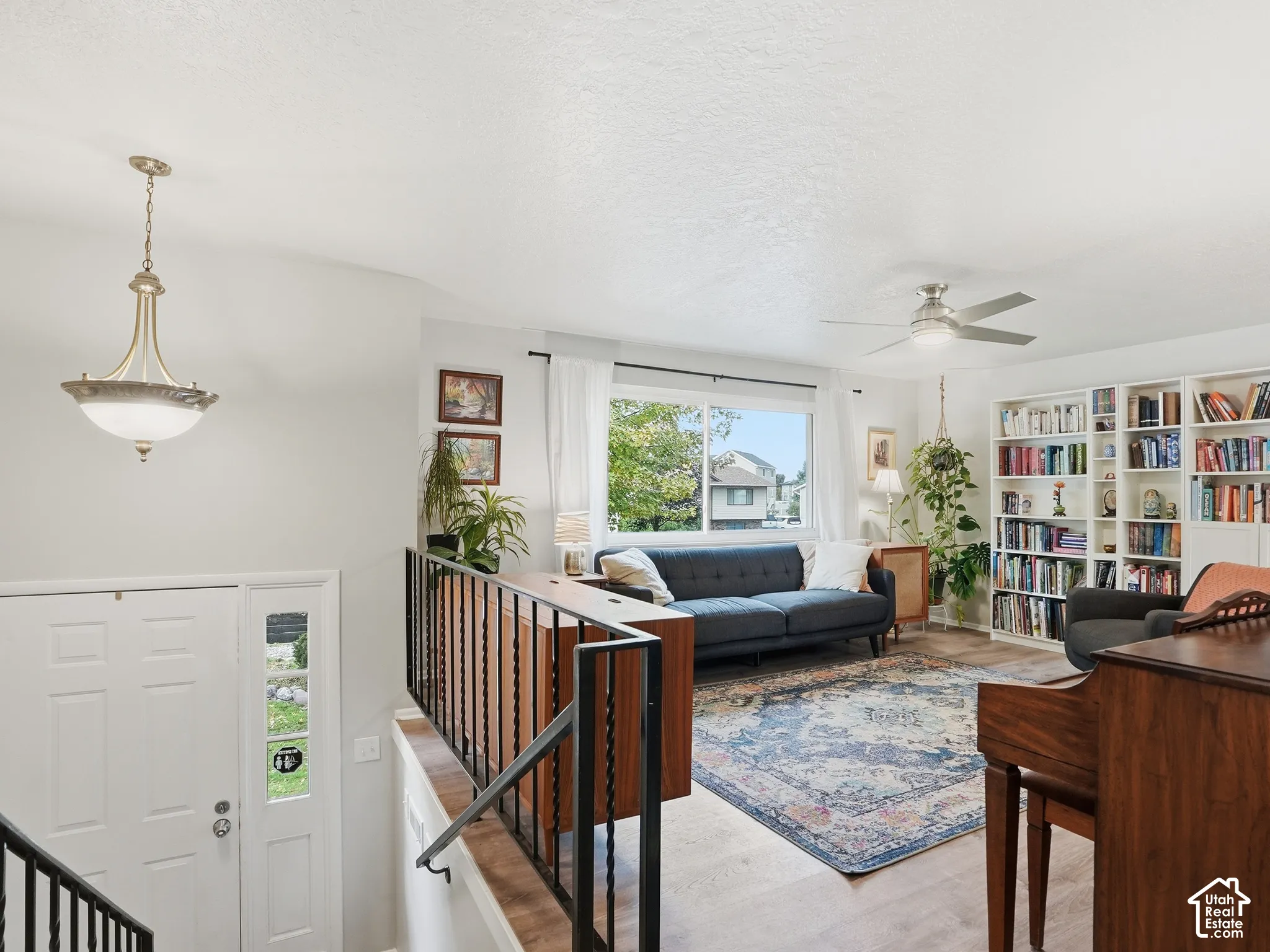 Living area featuring built-in floor-to-ceiling bookshelves, wood-finish flooring, metal railing, integrated ceiling fan, and pendant lighting