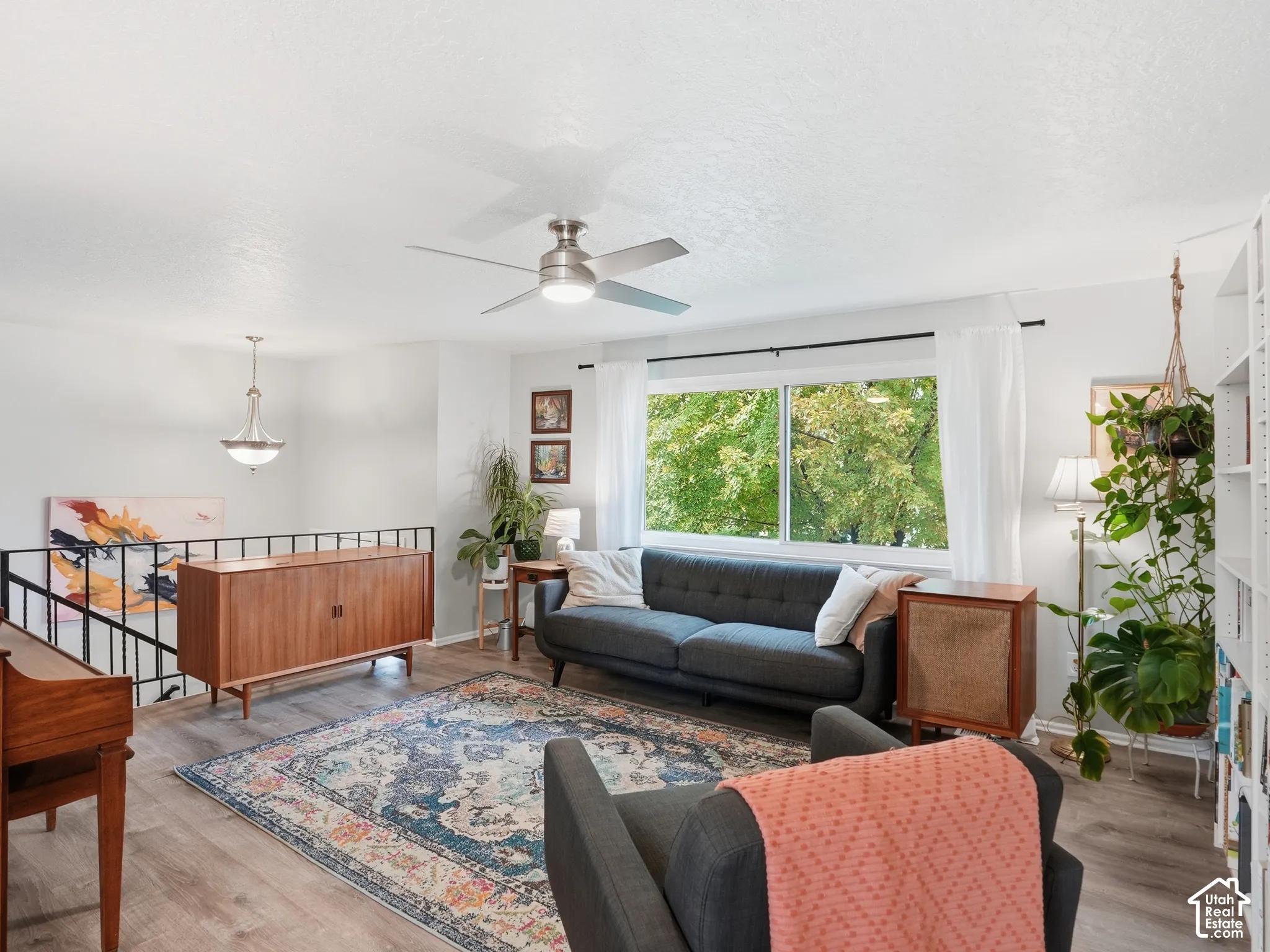 Living area featuring wood-finish flooring, a metal stair railing, a brushed nickel ceiling fan, and a pendant light fixture